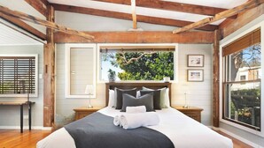 Un dormitorio con una cama grande, vigas de madera, una ventana con vistas a la vegetación y una mesita con una lámpara.