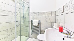 A bathroom with a glass shower enclosure, a white sink with a chrome faucet, and a towel rack with a white towel. - Ground Floor 2-Bed Near City Centre and Broadway (London)