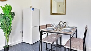 A dining area with a white refrigerator, a wooden table set for four, and a large mirror on the wall. - Ground Floor 2-Bed Near City Centre and Broadway (London)