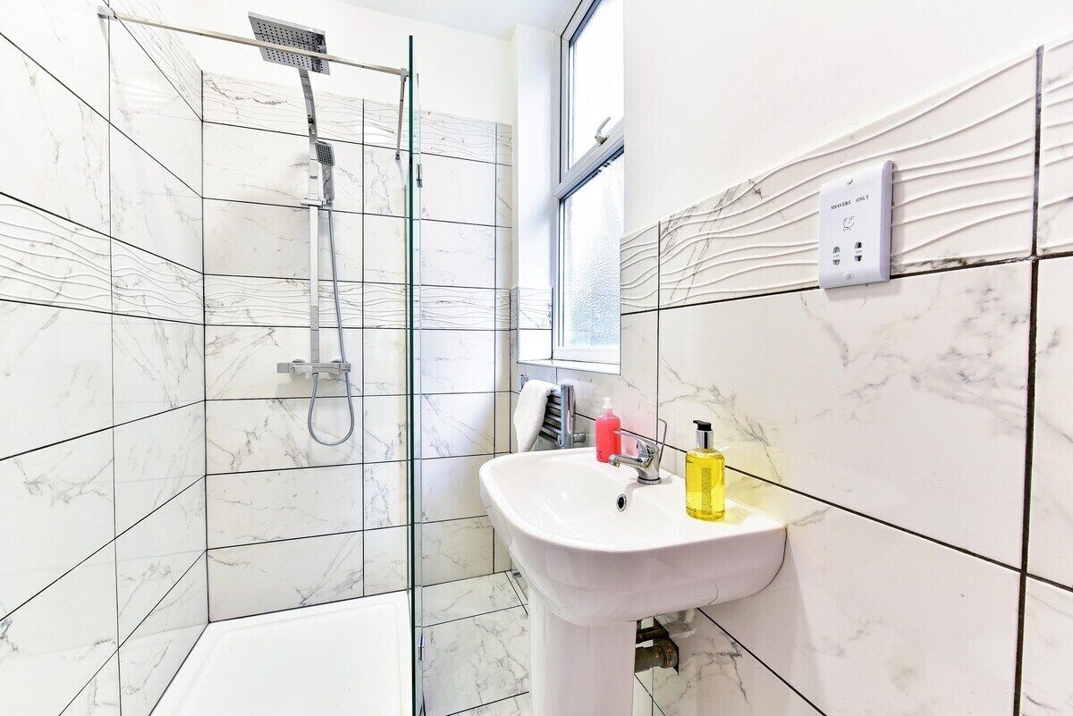 Een badkamer met douche, wastafel en raam.