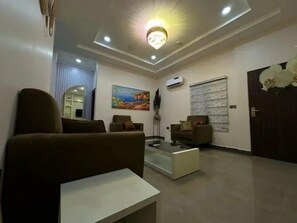 A modern living room with a sofa, coffee table, and a painting on the wall. - Billies Court (Abuja)