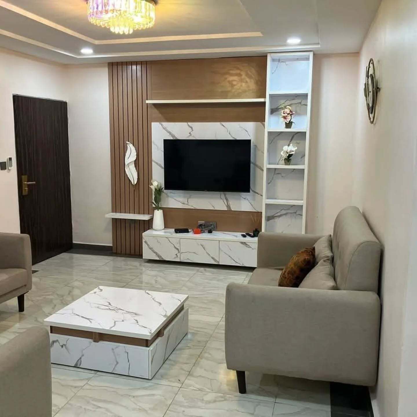 Una sala de estar moderna con una mesa de centro de mármol, un sofá, un televisor montado en una pared de mármol y una pared de acento de madera.
