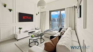 En moderne stue med et stort fjernsyn, der viser "NETFLIX", en sofa, et sofabord og udsigt til bybilledet gennem store vinduer.