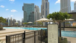 En swimmingpool med en bysilhuet i baggrunden, omgivet af moderne bygninger og parasoller.