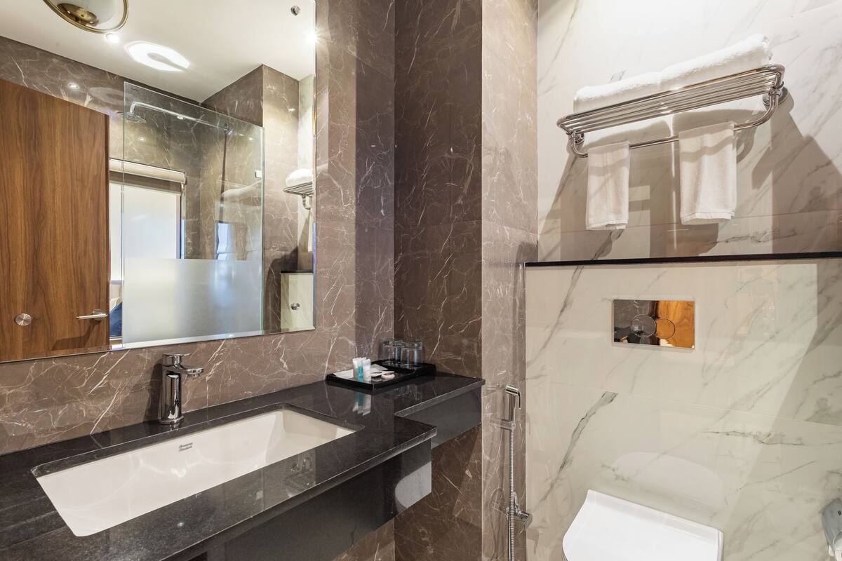Un baño moderno con un espejo grande, un lavamanos con encimera negra y una ducha con mampara de vidrio.