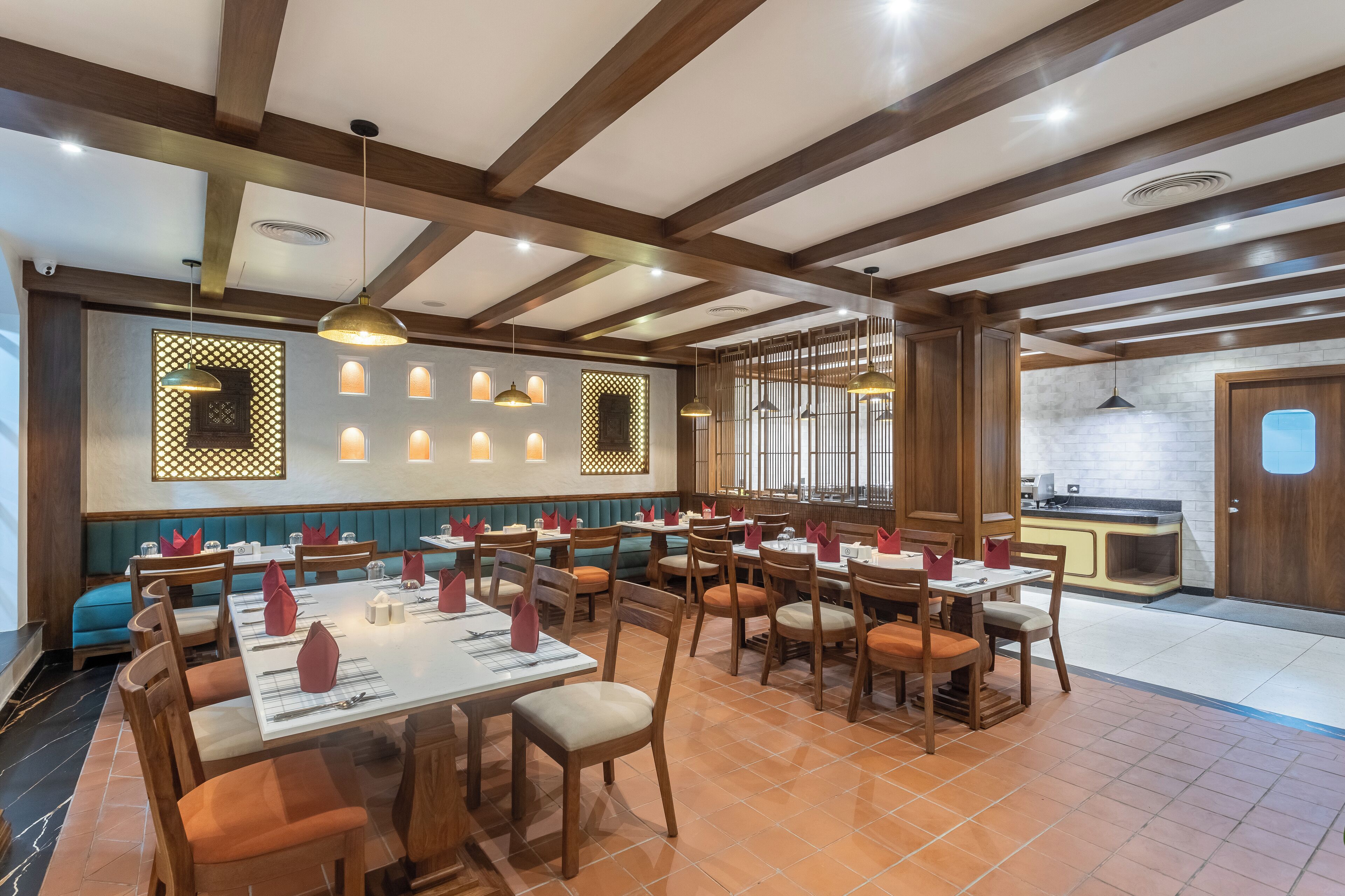 Un restaurante con vigas de madera, varias mesas y cabinas para comer, y una zona de cocina visible a través de un panel de vidrio.