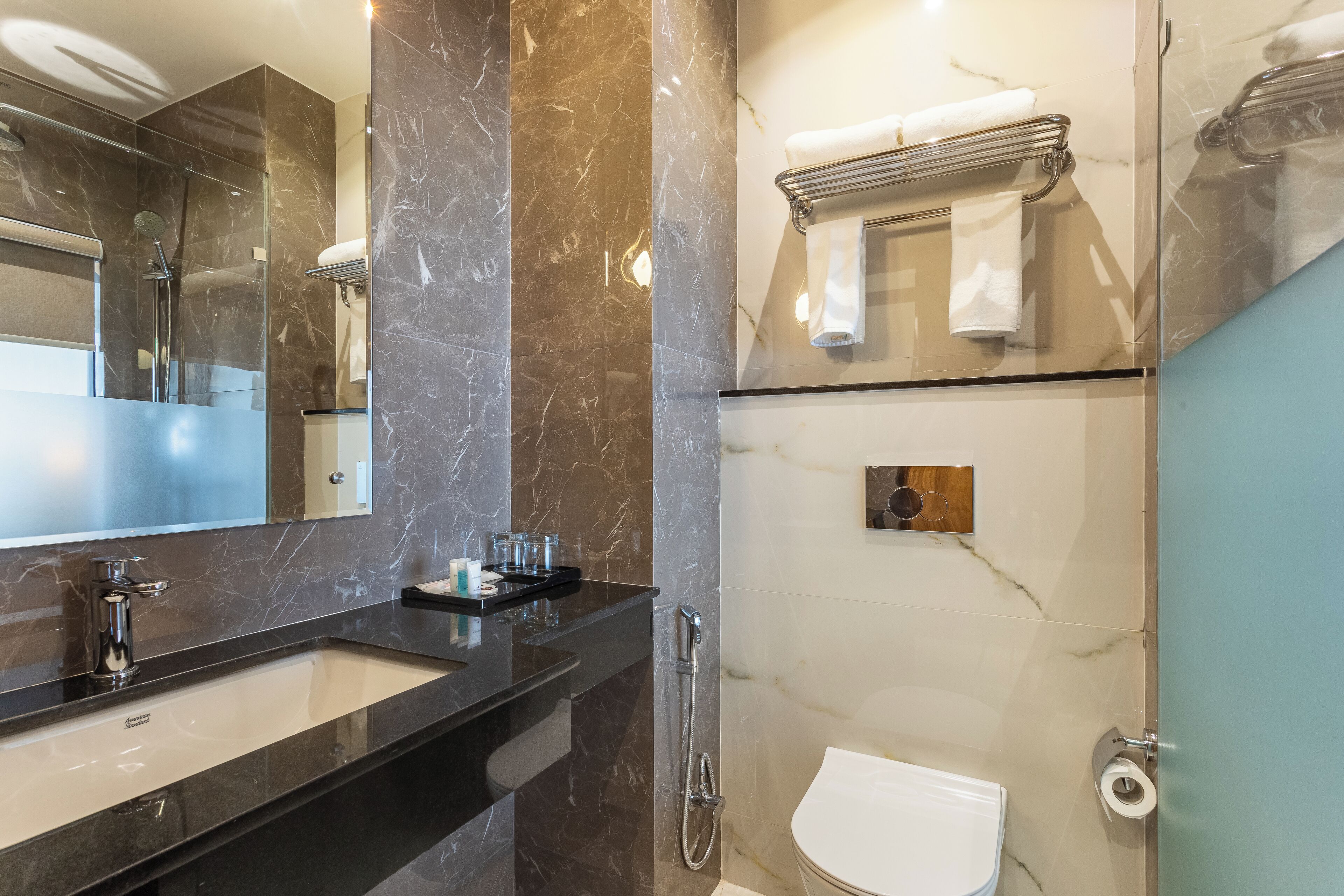 A modern bathroom with a large mirror, a black countertop, a white sink, a glass shower enclosure, and a toilet.