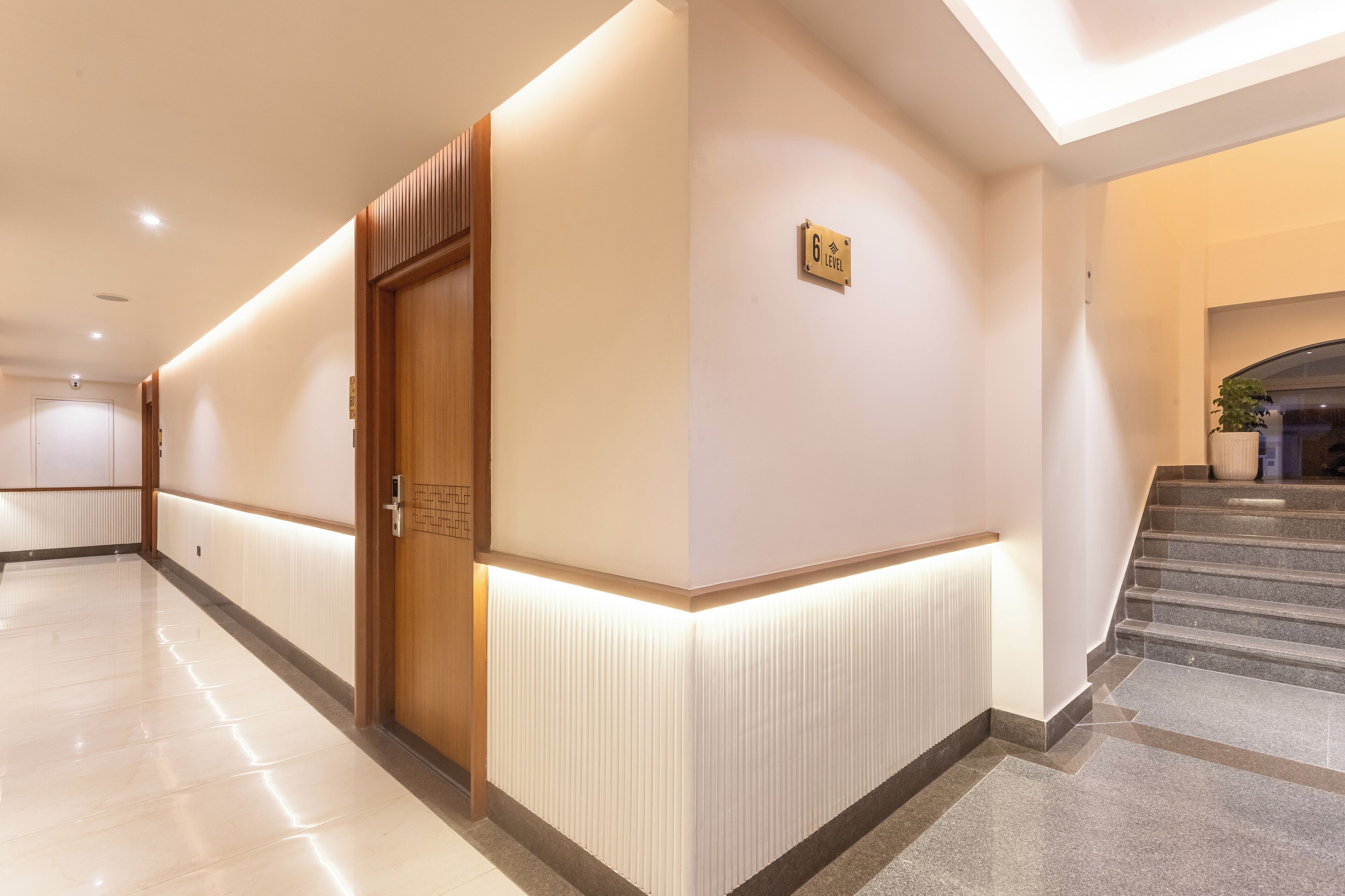 A modern hotel corridor with a wooden door, a sign indicating the 6th level, and a staircase leading to an upper floor.