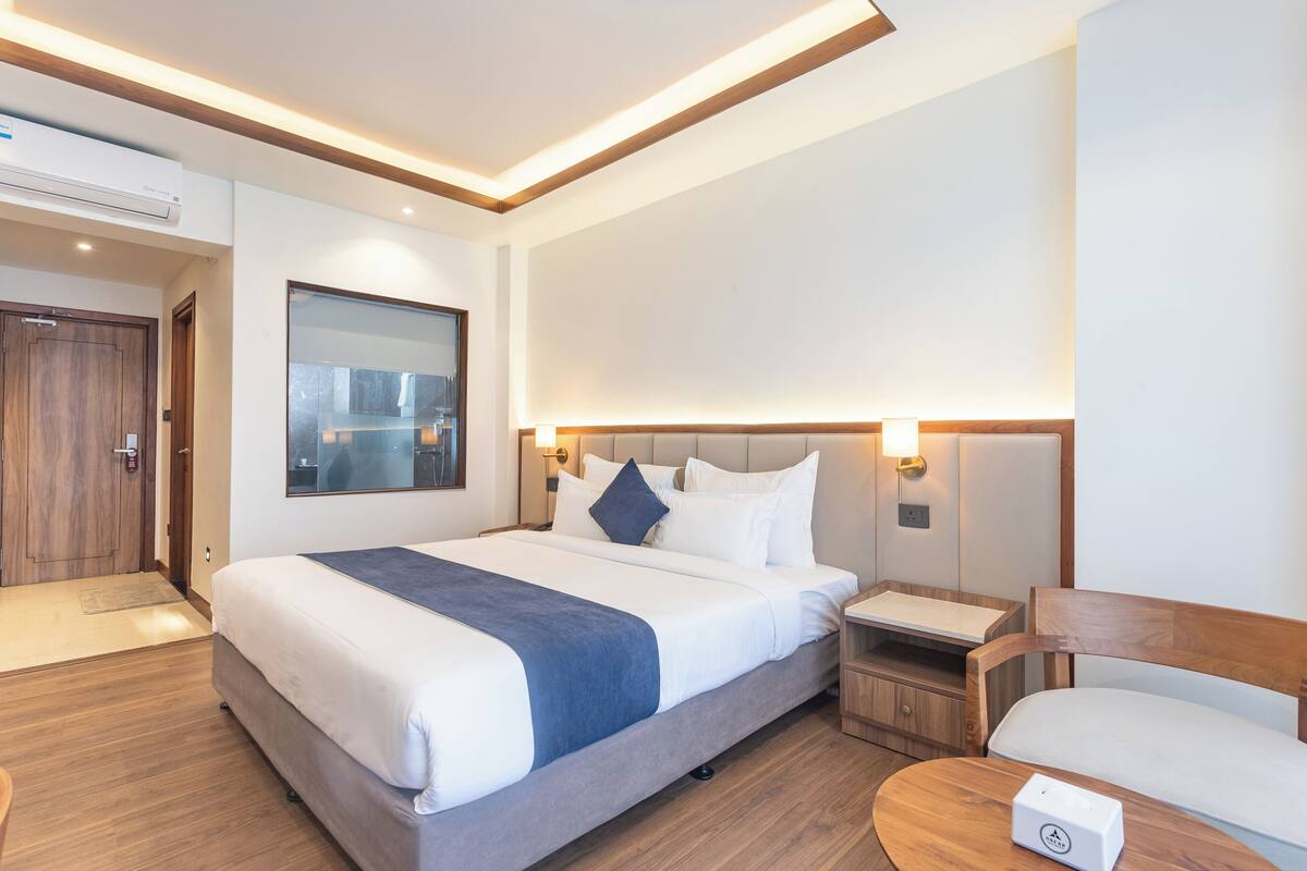 Una habitación de hotel moderna con una cama grande, suelo de madera, una mesita de noche, una silla y un aire acondicionado instalado en la pared.