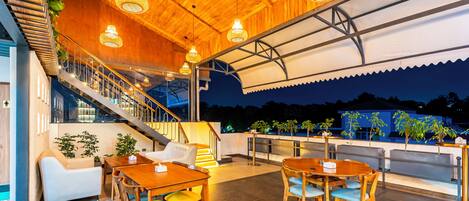 Un restaurante con mesas y sillas de madera, una escalera y vistas al cielo nocturno.