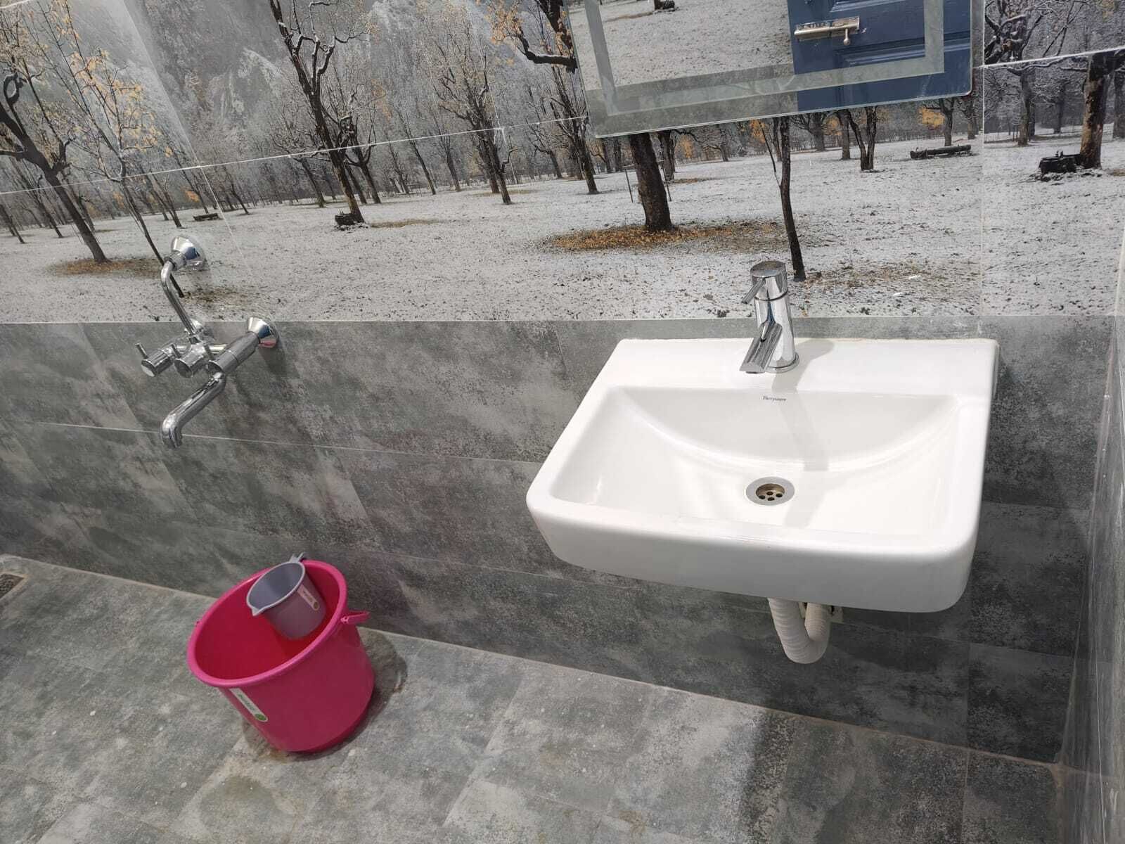 A public restroom with a white sink, a red bucket, and a metal handrail.