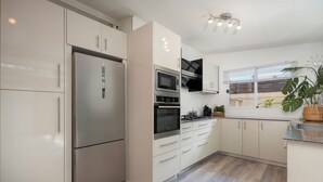 A modern kitchen with white cabinets, stainless steel appliances, and a window with blinds. - Modern Guesthouse with Private Pool • Close to Beaches, Shops & Restaurants • (Punaauia)