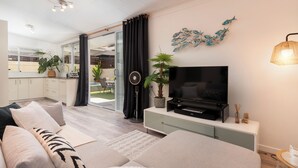 A modern living room with a sofa, TV, and potted plants. - Modern Guesthouse with Private Pool • Close to Beaches, Shops & Restaurants • (Punaauia)