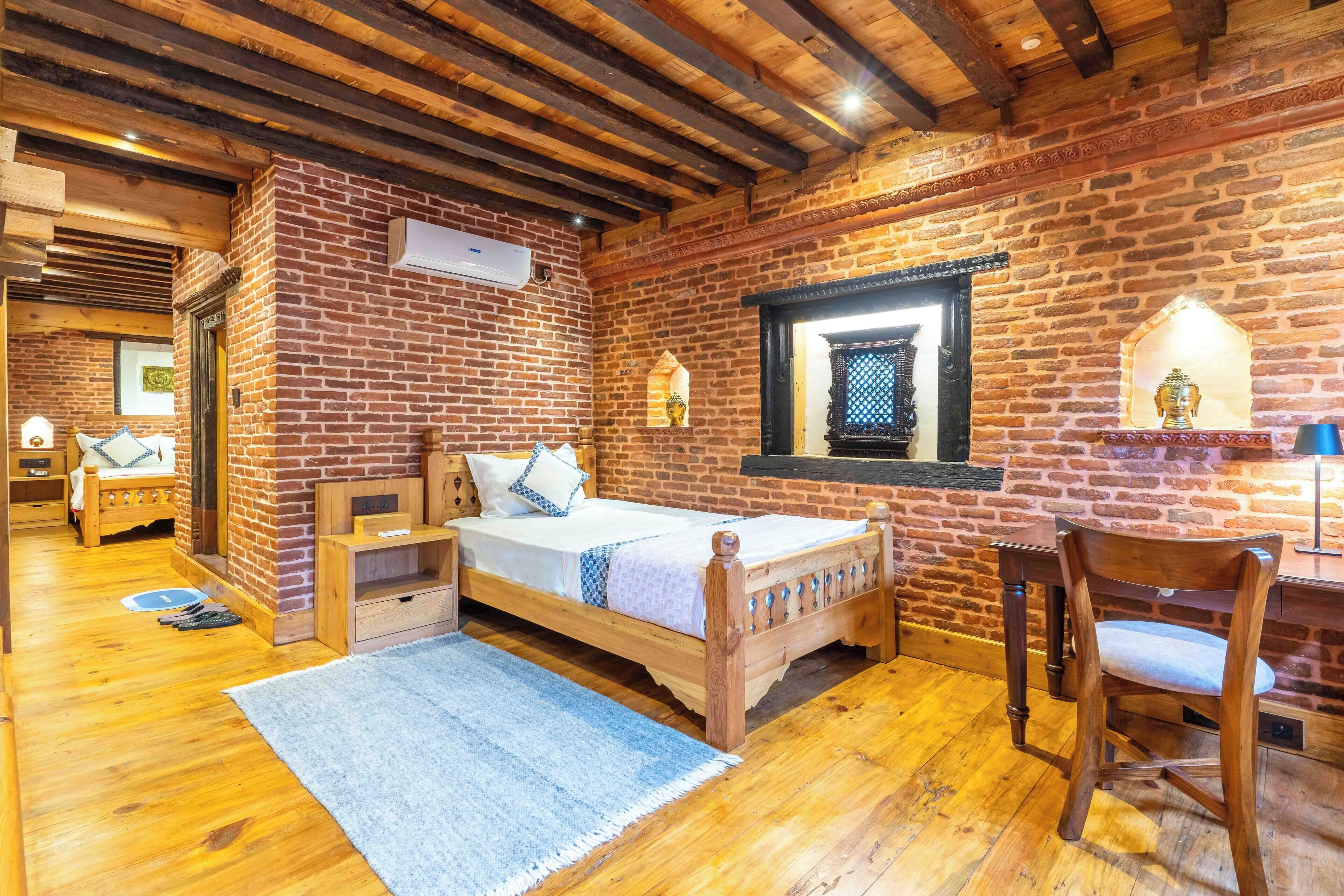 A rustic room with exposed brick walls, a wooden bed, a desk, and a chair.
