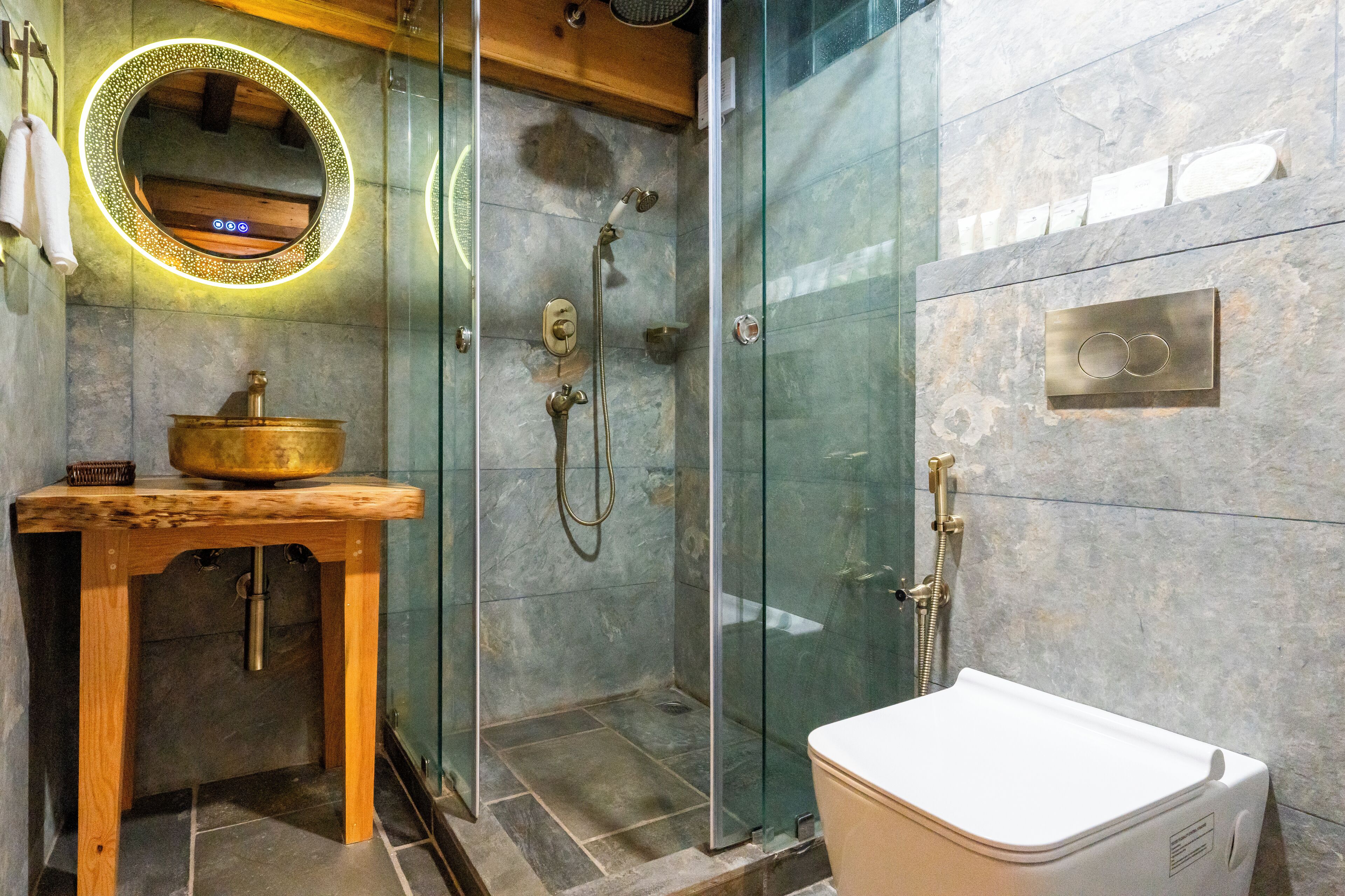 Un baño moderno con ducha envuelta en vidrio, tocador de madera con lavabo y un inodoro blanco.
