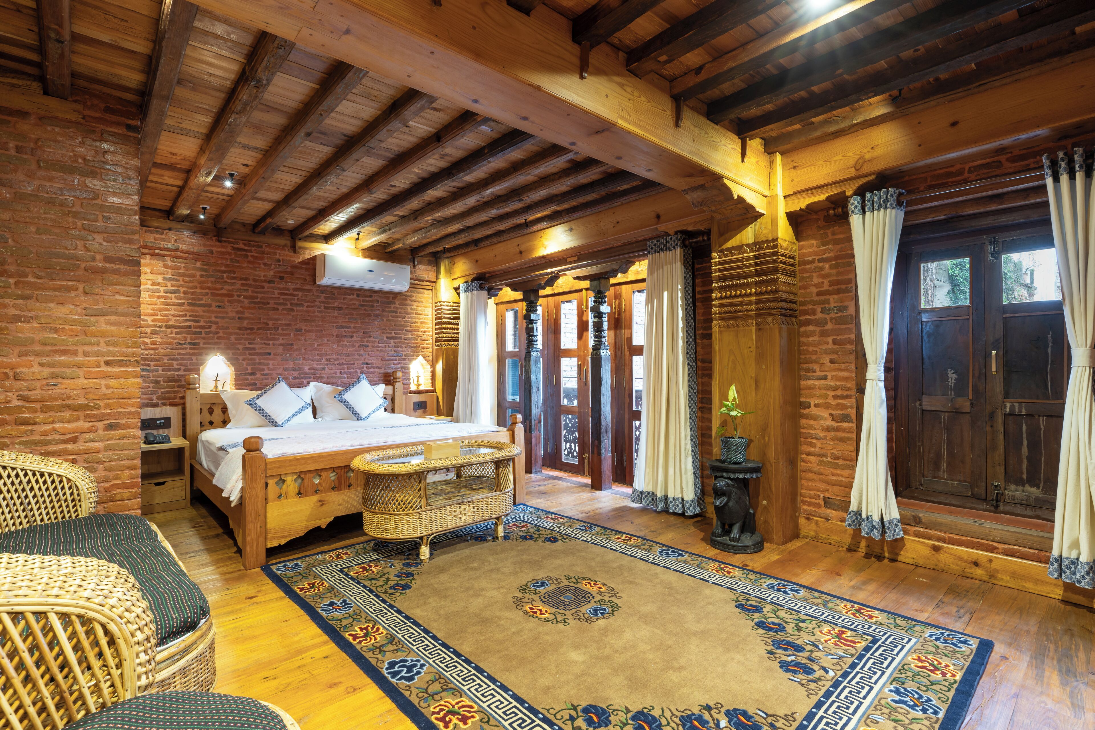 A cozy room with a wooden bed, wicker furniture, a patterned rug, and a brick wall.