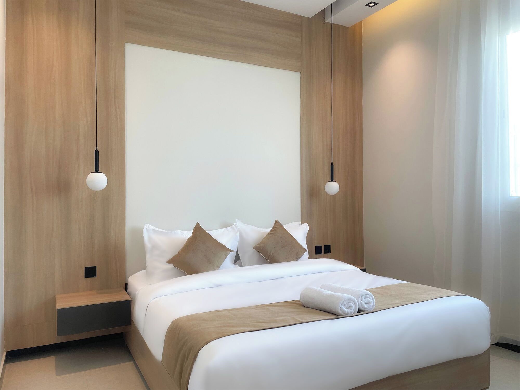 Una habitación de hotel moderna con cabecera de madera, ropa de cama blanca y dos lámparas fijadas a la pared.