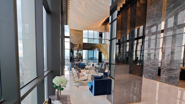 Een ruime lobby met een hoge plafond, grote ramen en een centrale trap.