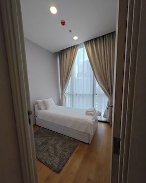 Un dormitorio moderno con una cama individual, un ventanal con cortinas y una alfombra pequeña.
