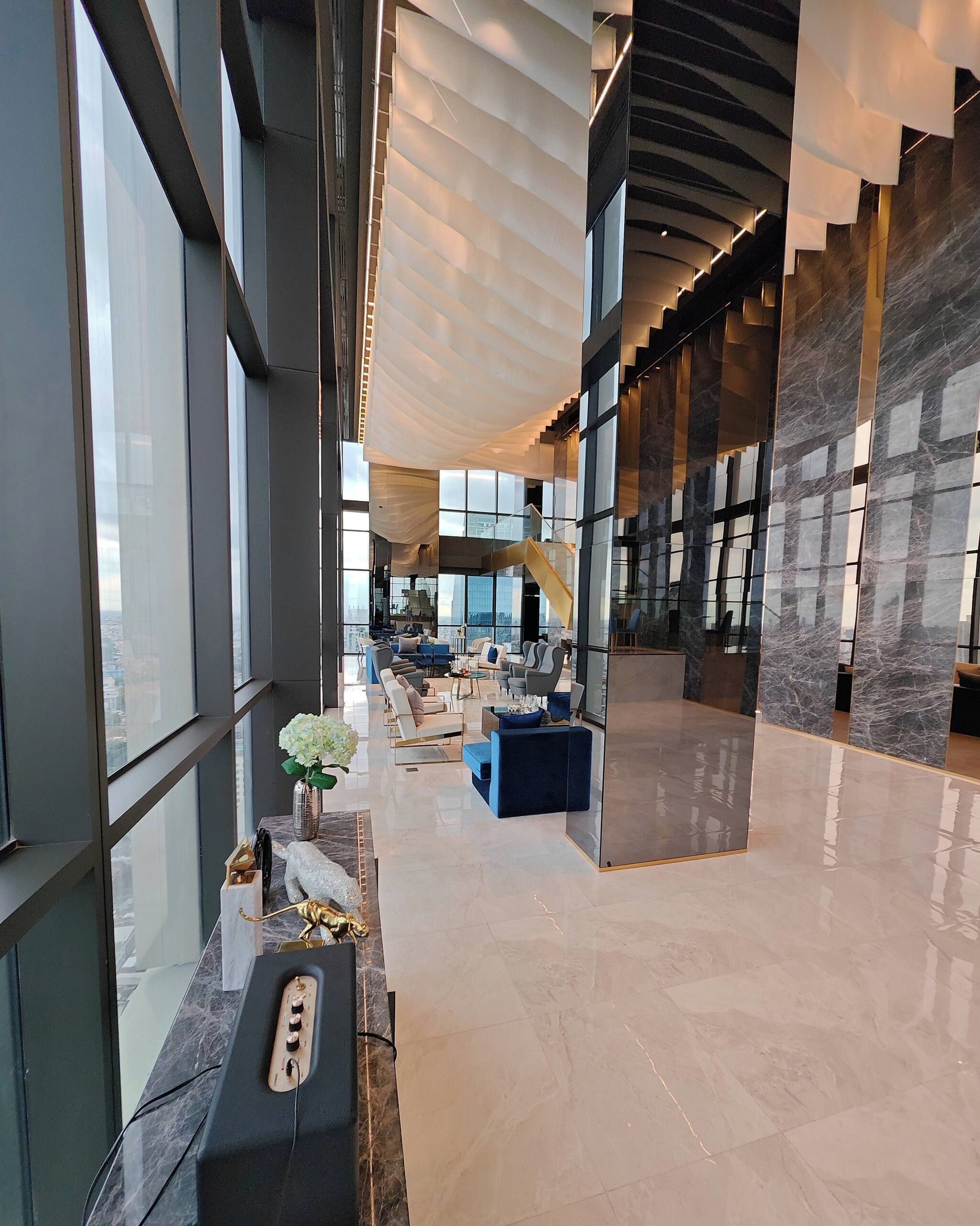 A spacious lobby with a high ceiling, large windows, and a central staircase.