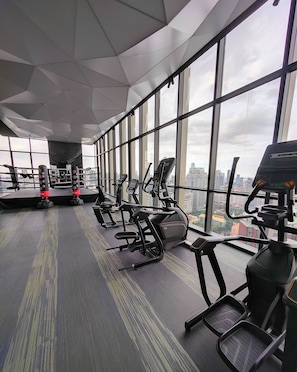 Un gimnasio con equipamiento de ejercicio, amplias ventanas y vista a la ciudad.