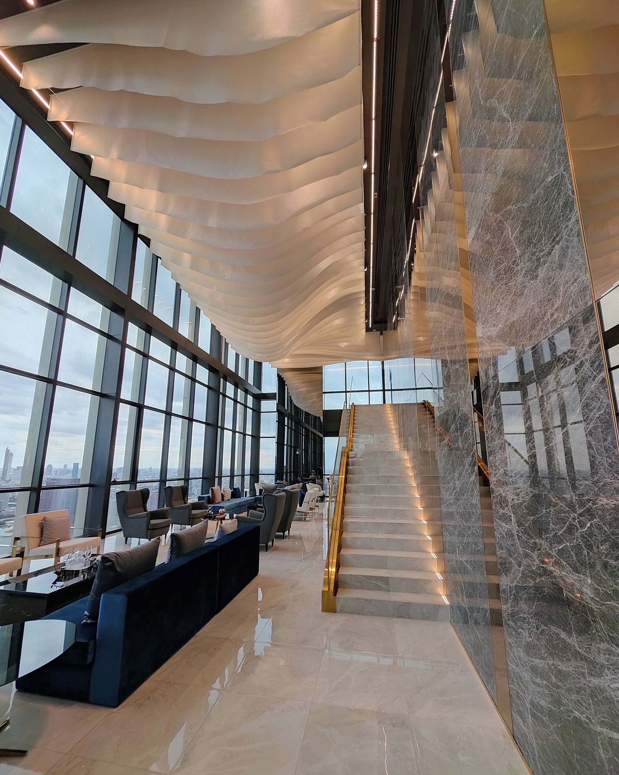 A modern interior with a curved ceiling, a marble staircase, and a seating area with sofas and tables.