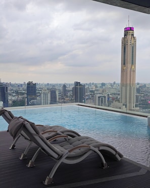 Una piscina en la azotea con sillones de descanso y vista panorámica de la ciudad.
