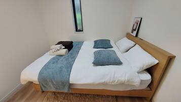 A neatly made bed with a wooden headboard, white and blue bedding, and a small window above it.