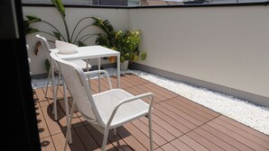 A small outdoor patio with a white table and two white chairs, surrounded by potted plants and a white pebble border.