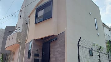 A modern two-story house with a flat roof, a black front door, and a small balcony.