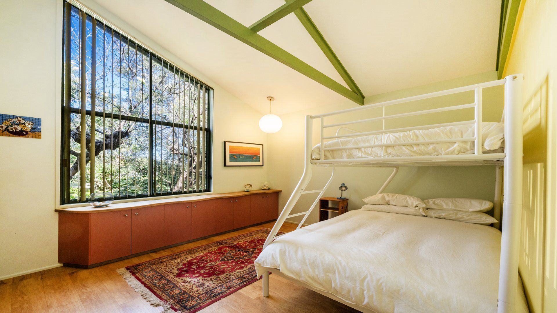 A bunk bed room with a window, a desk, and a rug.