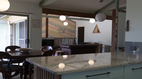 A modern kitchen with a marble countertop, a dining area with a table and chairs, and a living area with a sofa and a television. - Magic Beach - Lifestyle Minnie Water (MINNIE WATER)