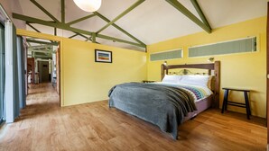 Ein Schlafzimmer mit einem hölzernen Bett, einem kleinen Nachttisch und Blick auf einen Flur.