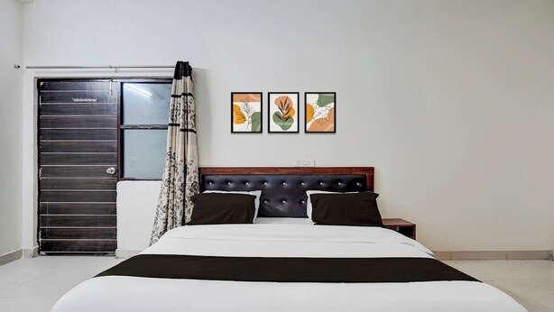 A bedroom with a bed, a nightstand, a wardrobe, and three framed artworks on the wall. - Hotel Heaven Peacock Noida (Noida)