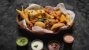 A basket of fried snacks and two small glasses of sauce on a dark surface. - Hotel Heaven Peacock Noida (Noida)