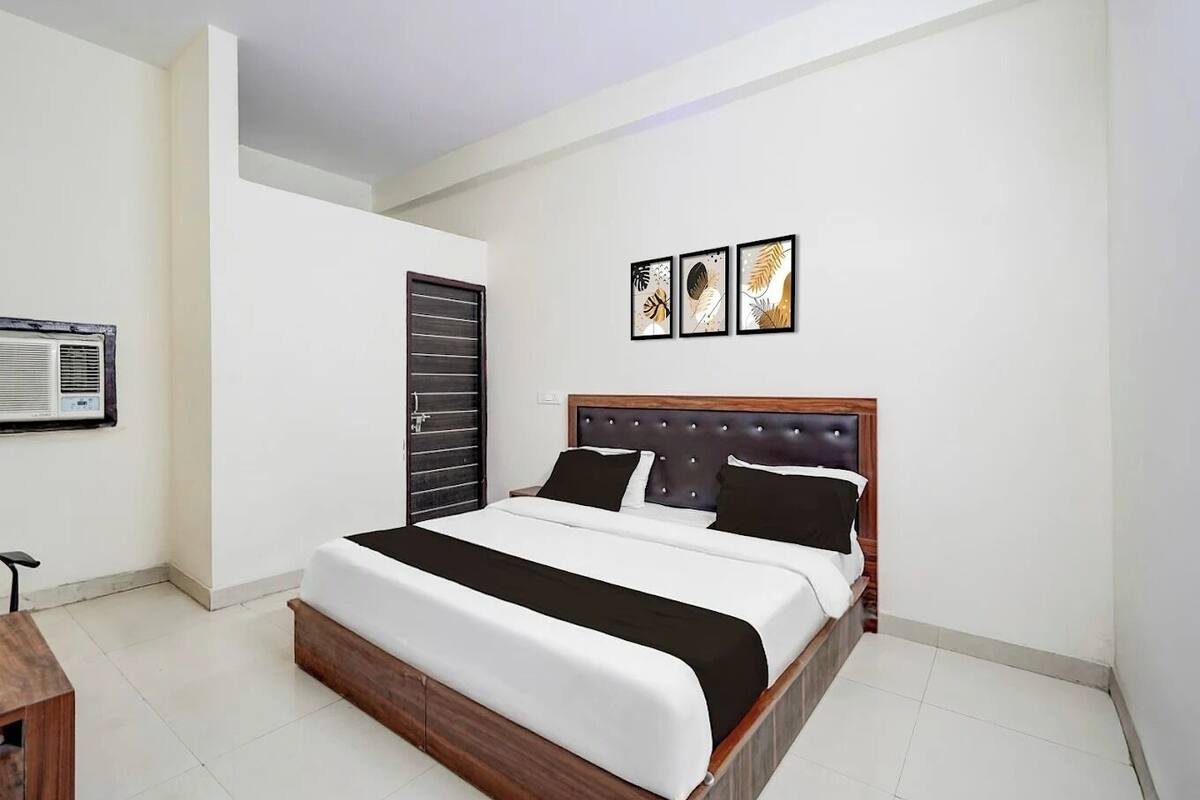 Una habitación de hotel con una cama grande, un cabecero de madera, un aire acondicionado instalado en la pared y tres cuadros enmarcados sobre la cama.