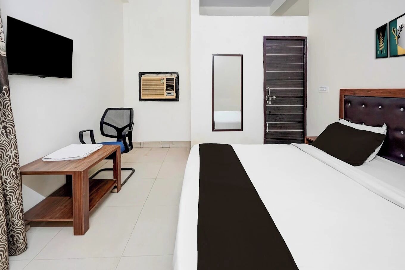 A modern hotel room with a bed, a desk, a chair, a TV, a mirror, and a wardrobe.