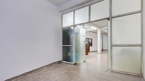 A hallway with a glass door leading to a room, a wooden floor, and a white wall. - Hotel Heaven Peacock Noida (Noida)