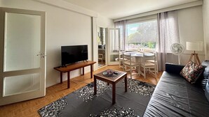 A living room with a TV, a dining table with chairs, a sofa, and a fan.