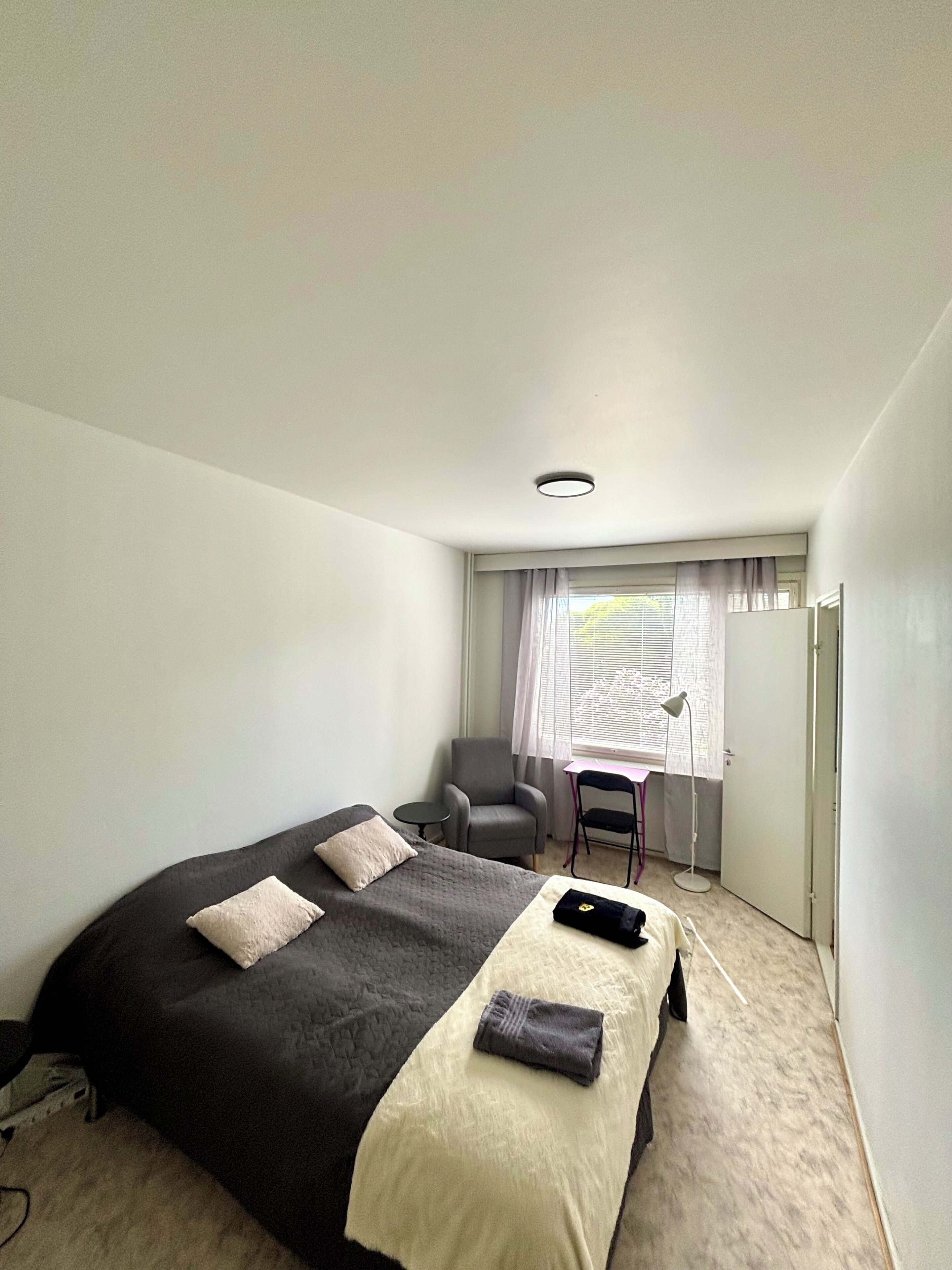 Hotellihuone, jossa on sänky, tuoli, työpöytä ja ikkuna, jossa on verhot.