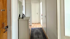 A hallway with a wooden door, a white cabinet, a red pendant light, and a patterned rug.