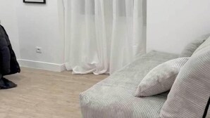 Ein Zimmer mit einer weißen Couch, einem schwarzen Mantel, der an der Wand hängt, und transparenten Vorhängen.