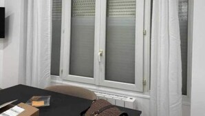 Ein Zimmer mit Fenster, Tisch und Stuhl. Auf dem Tisch steht eine Schachtel.