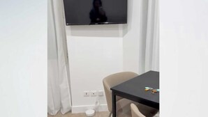 Ein Zimmer mit einem an der Wand befestigten Flachbildfernseher, einem kleinen Tisch mit einer Brille darauf und einem Sessel.