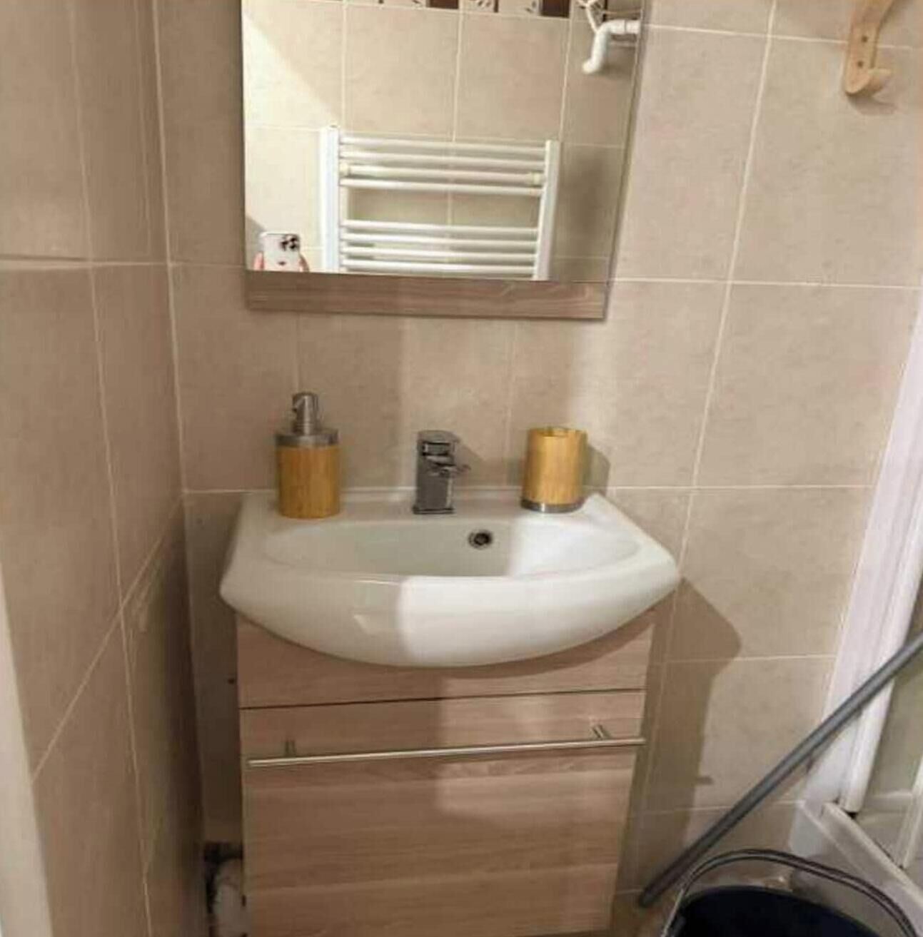 A bathroom with a white sink, wooden handles, a mirror above, and beige tiles.