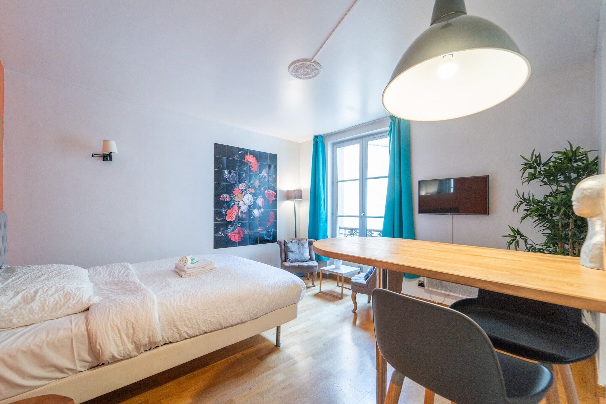 A modern bedroom with a bed, a desk, a chair, a TV, and a window with curtains.