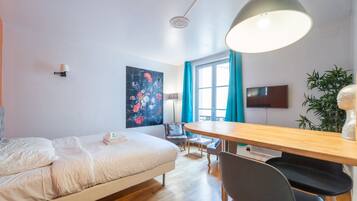 A modern bedroom with a bed, a desk, a chair, a TV, and a window with curtains.
