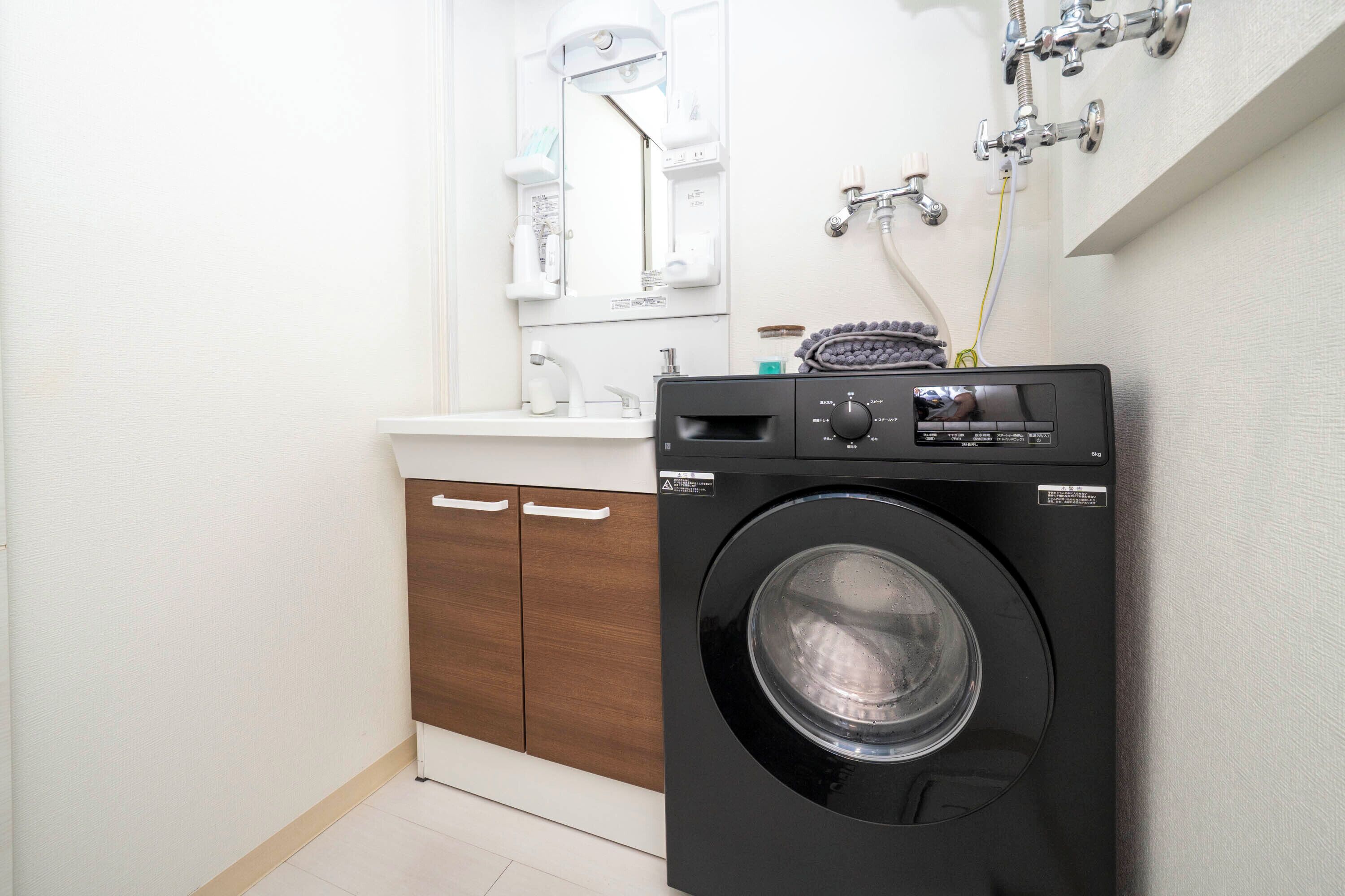 Un baño moderno y funcional, con lavadora y secadora integradas, muebles de madera y encimera blanca.