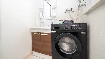 Un baño moderno y funcional, con lavadora y secadora integradas, muebles de madera y encimera blanca.