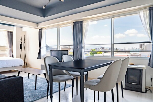 A modern hotel room with a large window, a dining table with chairs, a bed, and a standing heater. - HILLSGARDEN 405 (Sapporo)